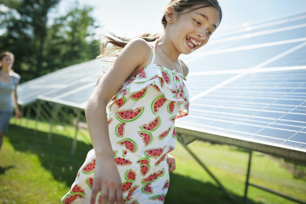 A child and her mother running beside solar panels.